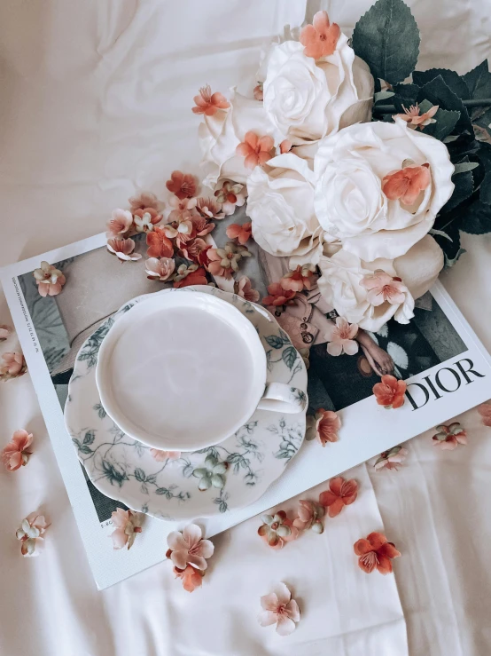 a white cup and saucer on a white and floral cloth