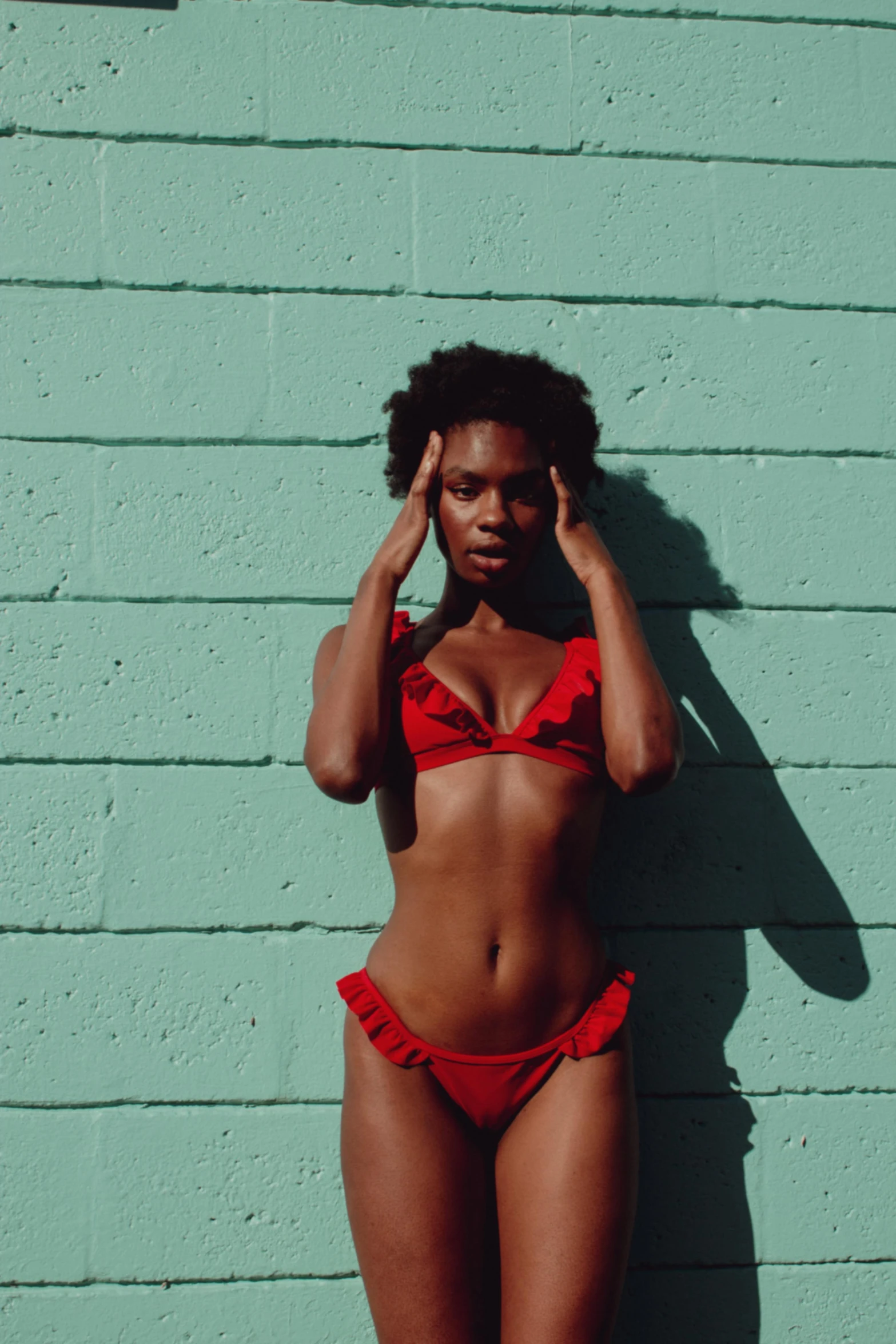 young lady in bikini against green brick wall