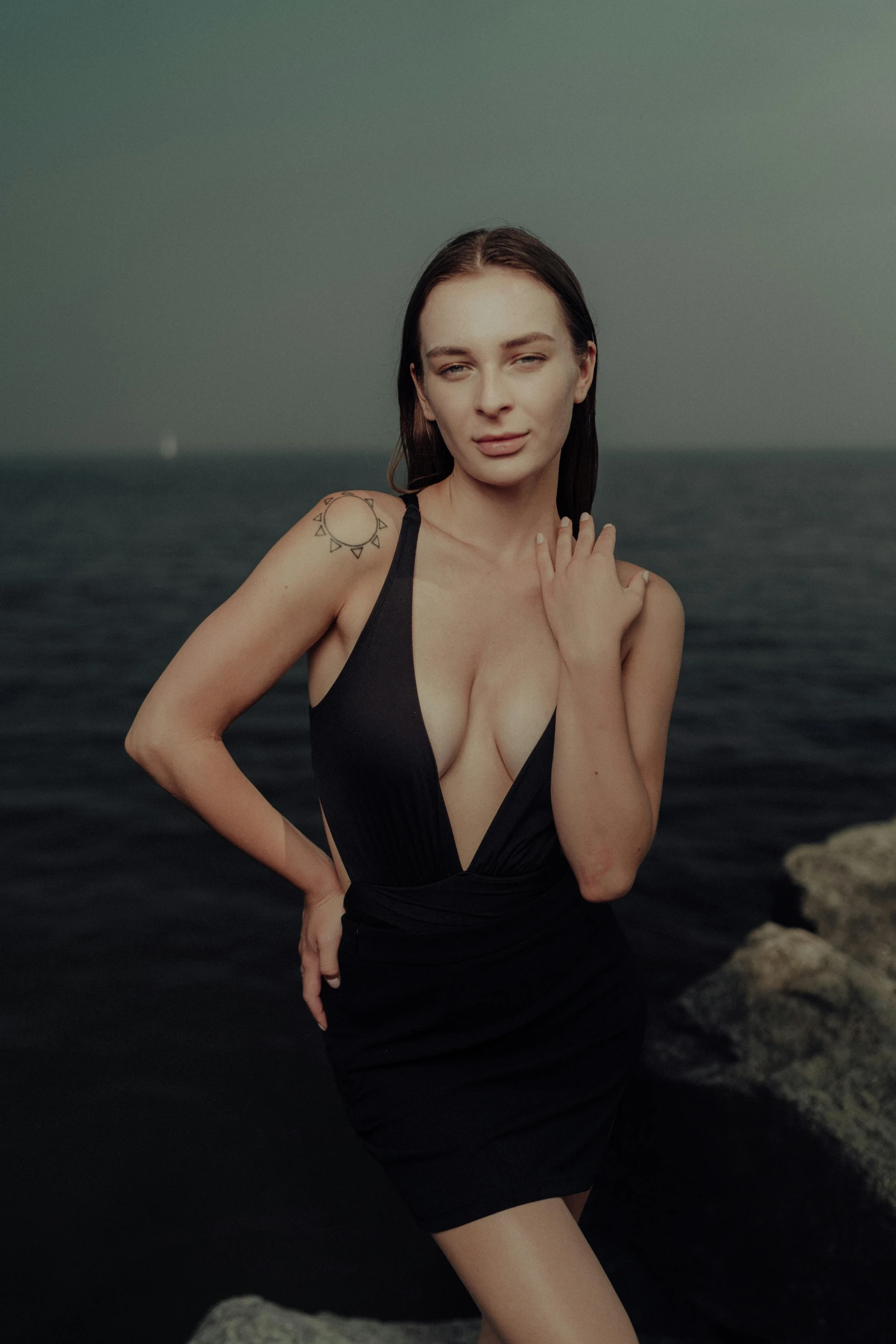 a woman in black is posing by the ocean