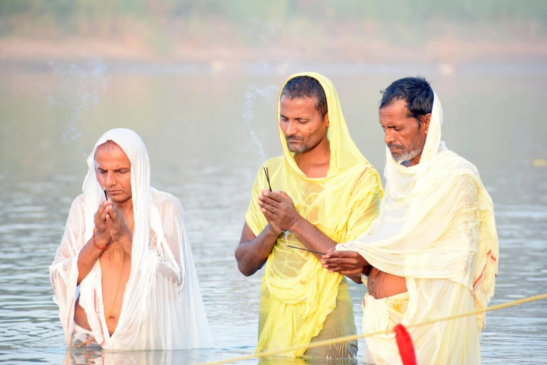 three men are on the side of a body of water and a person is wearing a yellow robe