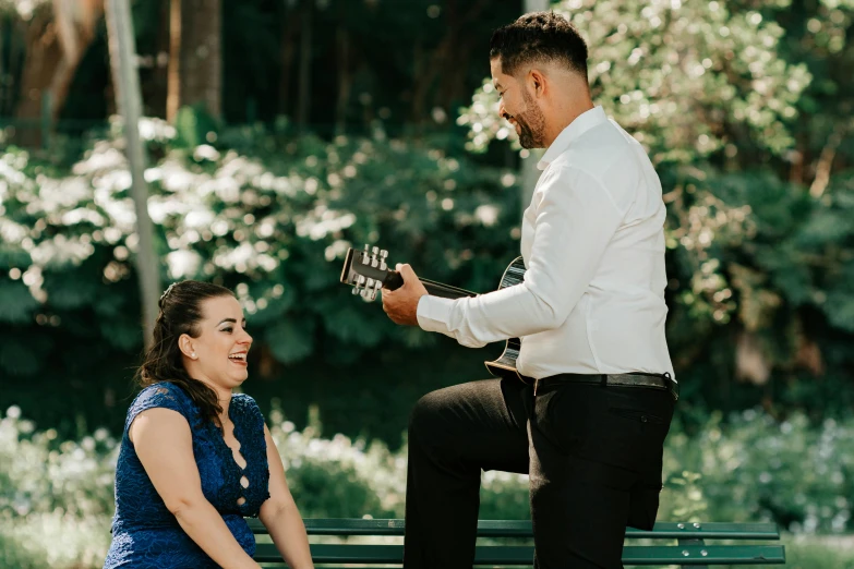 a woman sitting on a bench with her guitar in her hand while a man sits beside her and plays the guitar