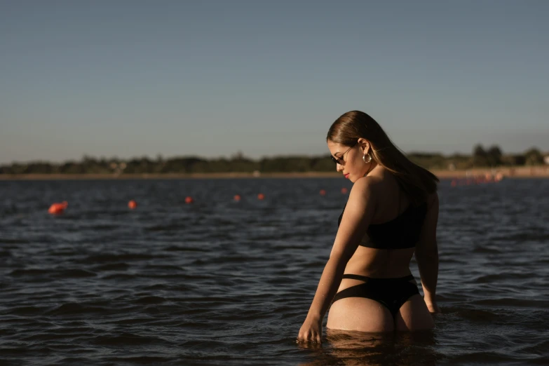 a girl in bikini and sunglasses sits in the water