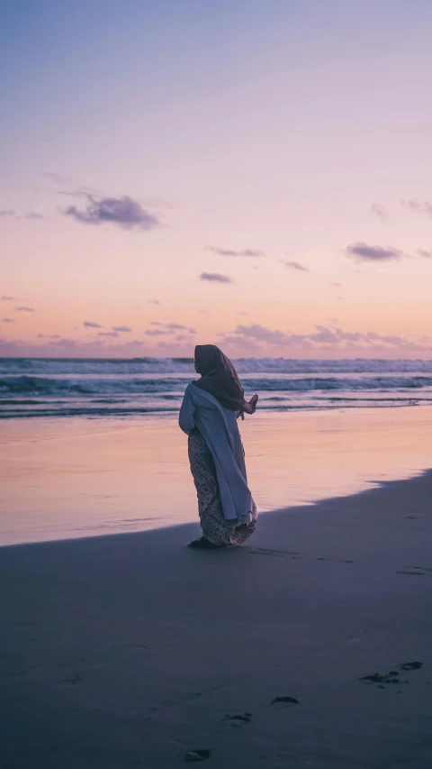 woman on beach with blanket over head with footprints in sand