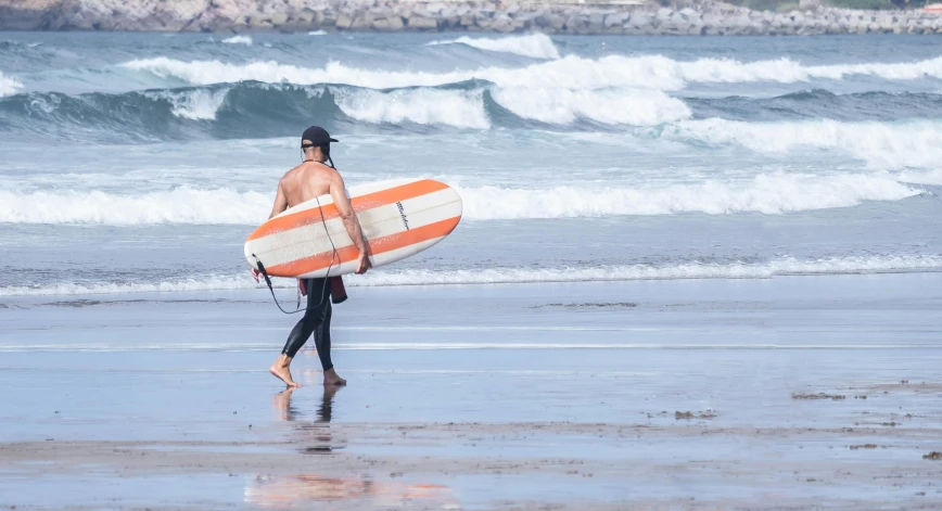 man with orange and white surfboard on ocean beach