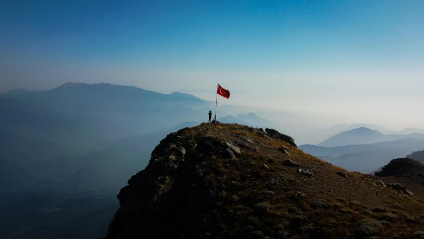 a person with a flag stands on top of a mountain