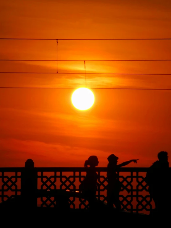 the sun sets over the top of a bridge while two people walk on the bridge