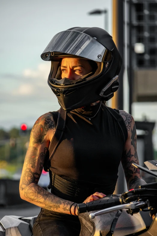 woman with tattooed arms, helmet and motorcycle gear, is driving her horse