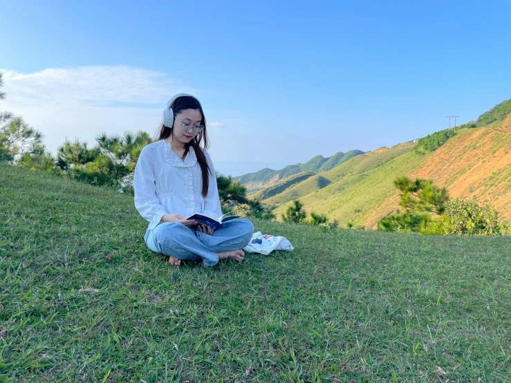 a young woman sitting in the grass on a hill