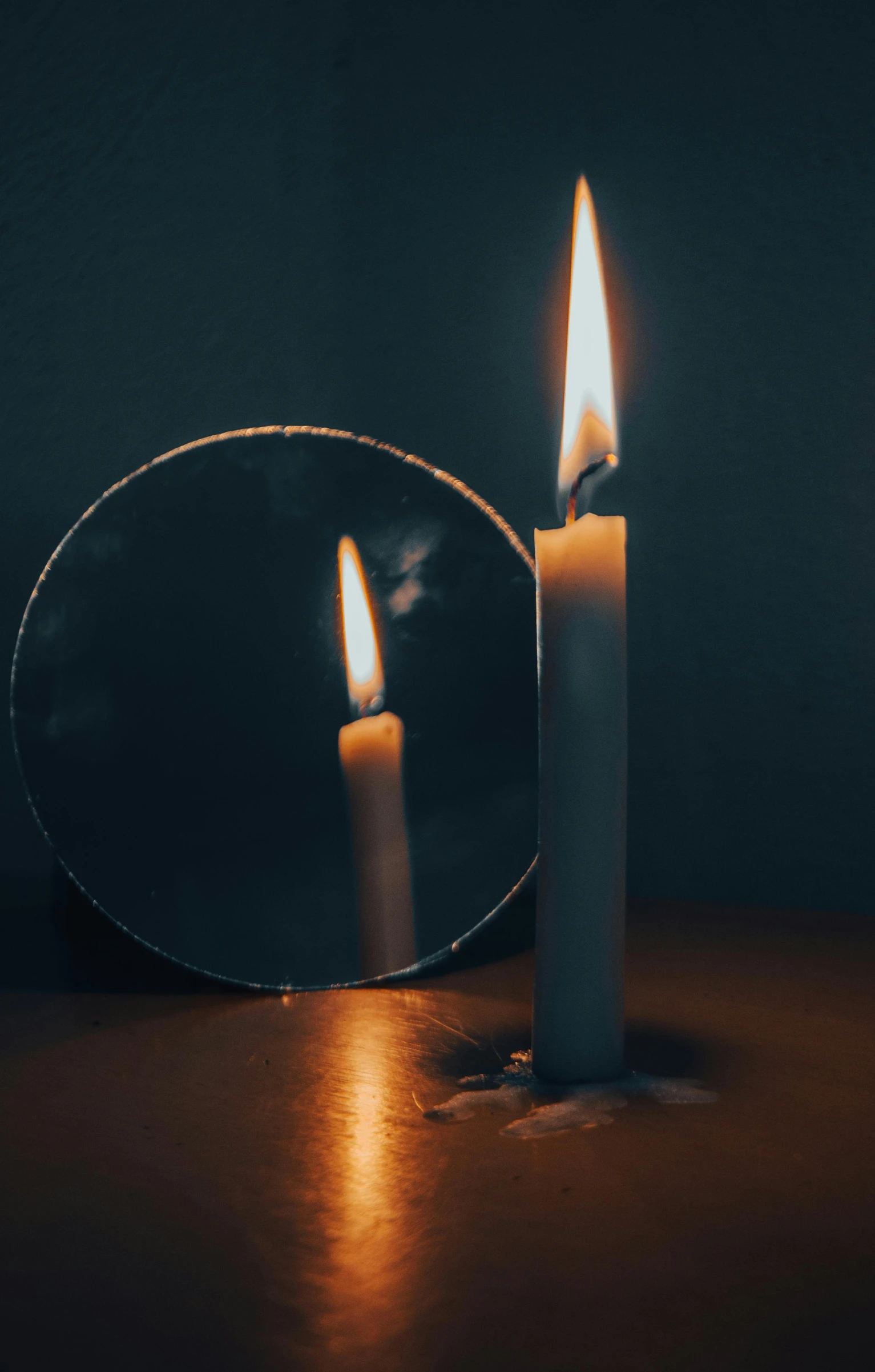 two lit candles stand next to an oval mirror