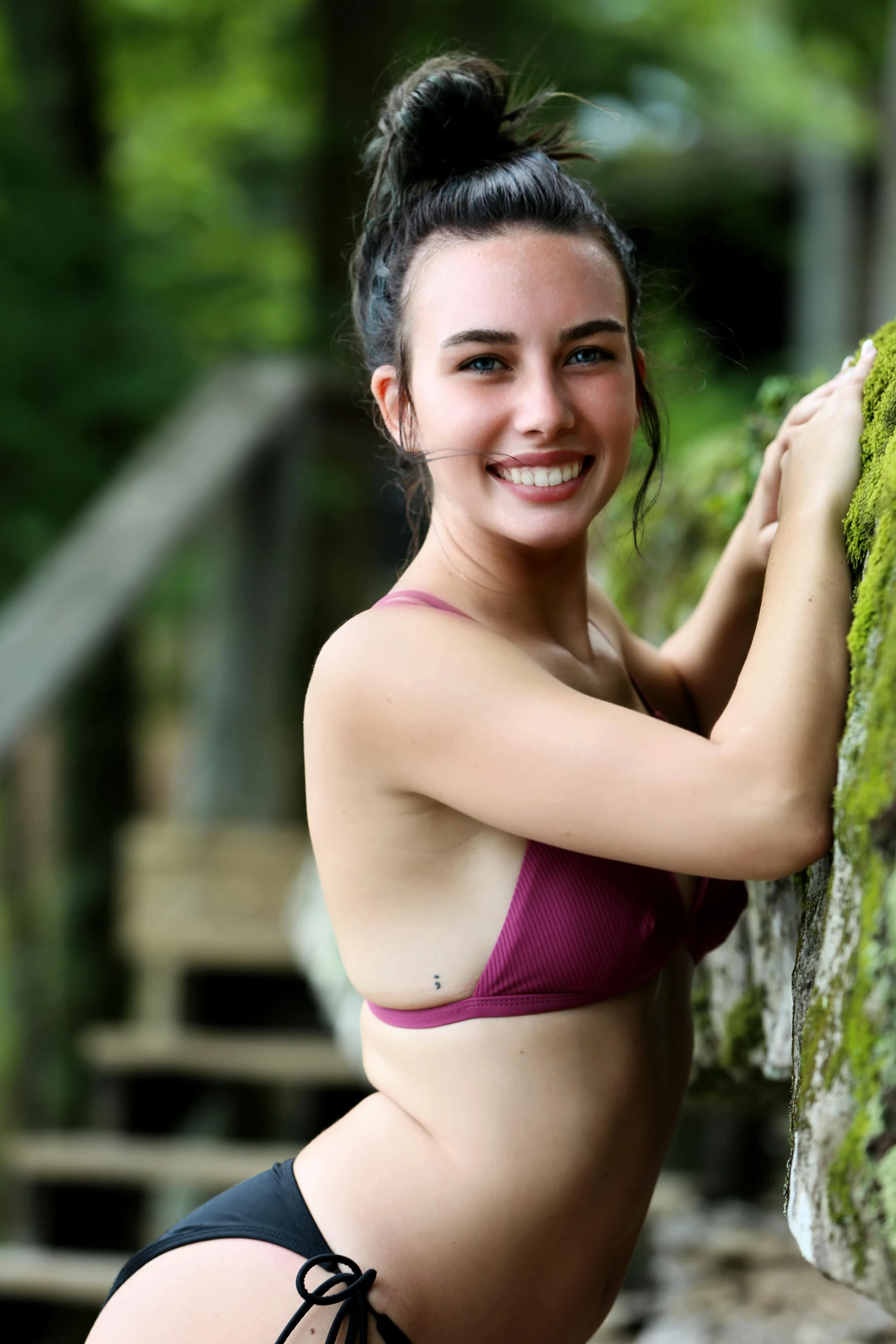 a beautiful young woman in a purple bikini standing next to a tree