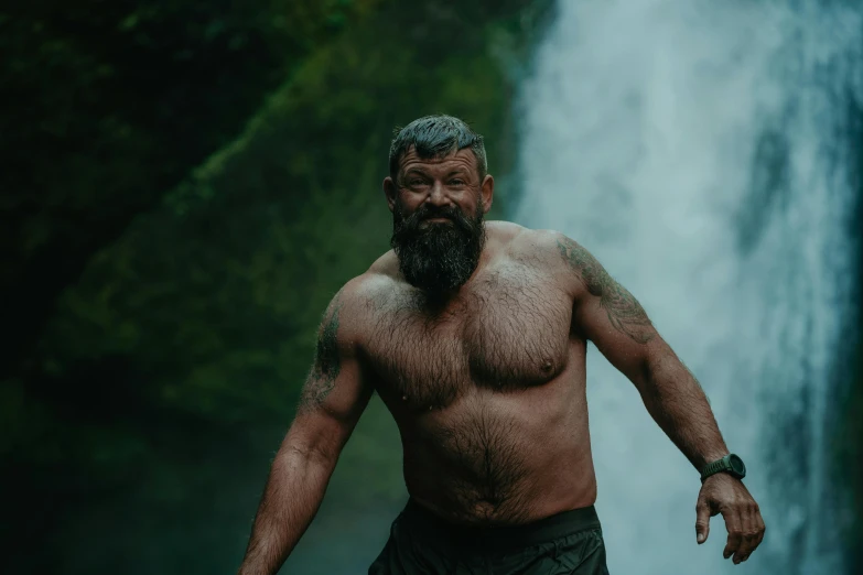 a bearded man standing in front of a waterfall