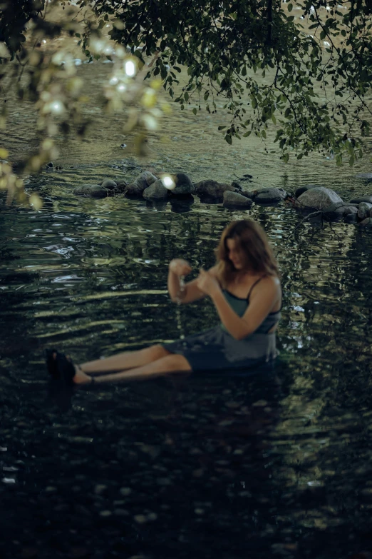 a woman sits in the water while holding a cell phone