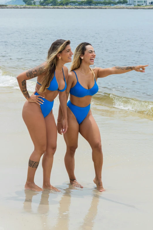 two women in blue swimsuits standing on the beach