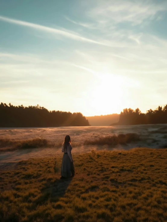 a woman stands alone in a field of grass at sunset