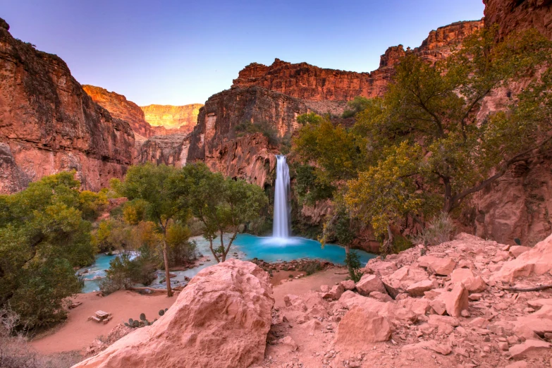 a waterfall sits on a rocky bank next to trees and a lake