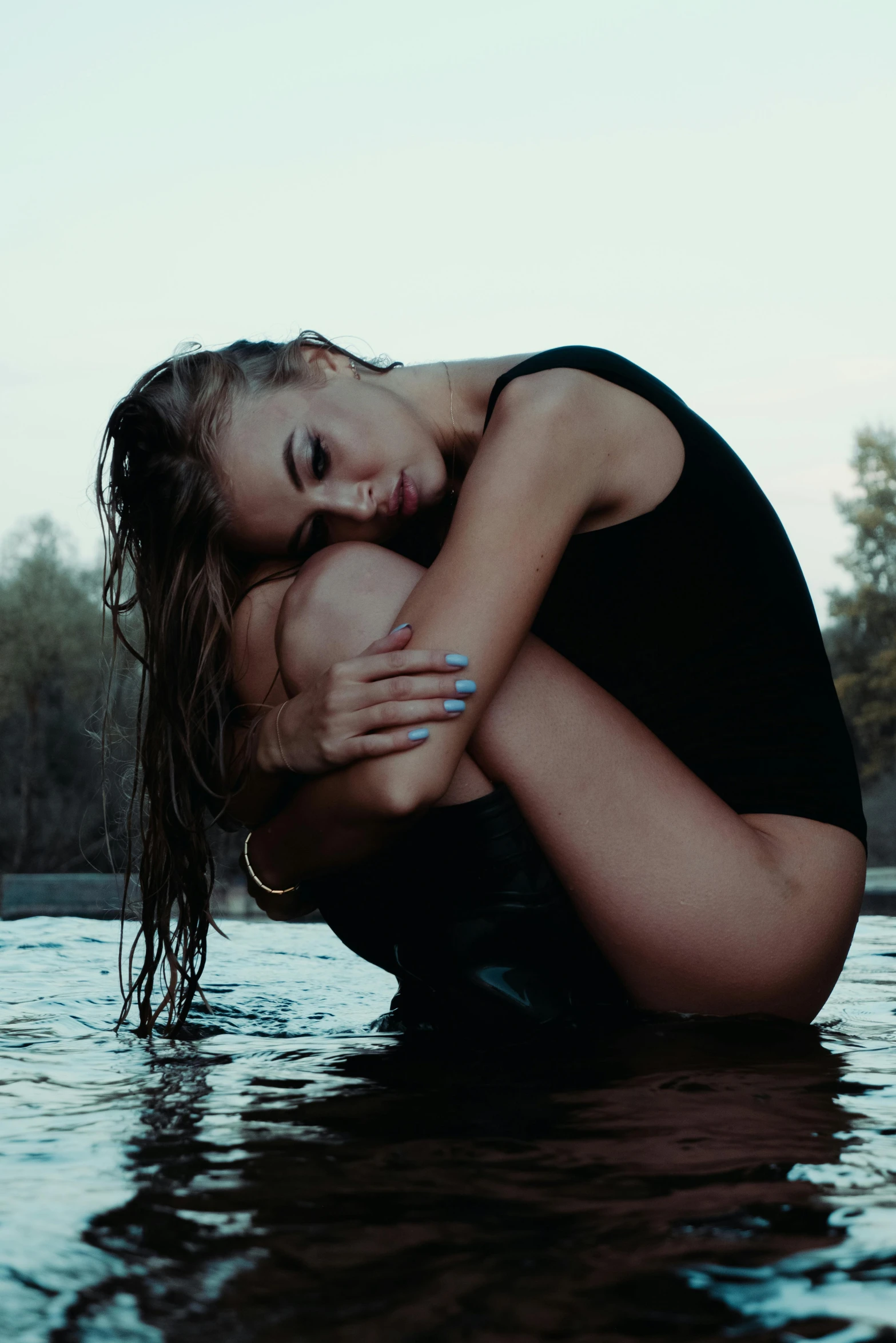 a girl in boots sits by the side of a body of water