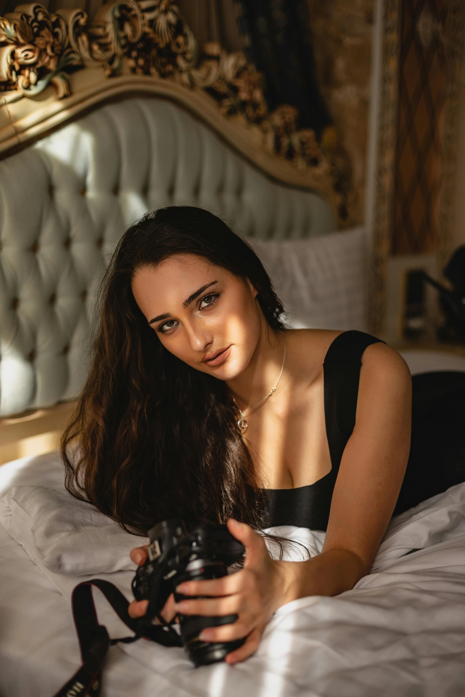 a woman with long dark hair lying in bed holding her camera