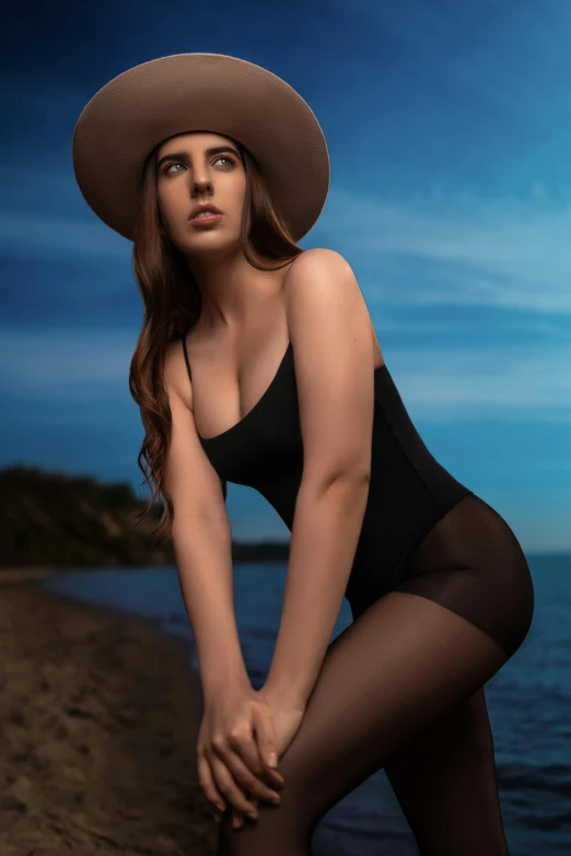 a woman in a swimsuit, hat and stockings posing on a beach