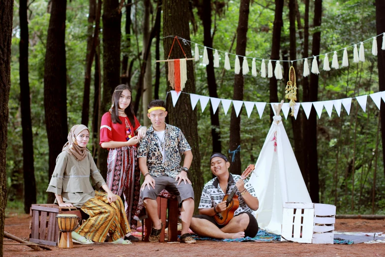 a group of people sit in the woods next to a teepee