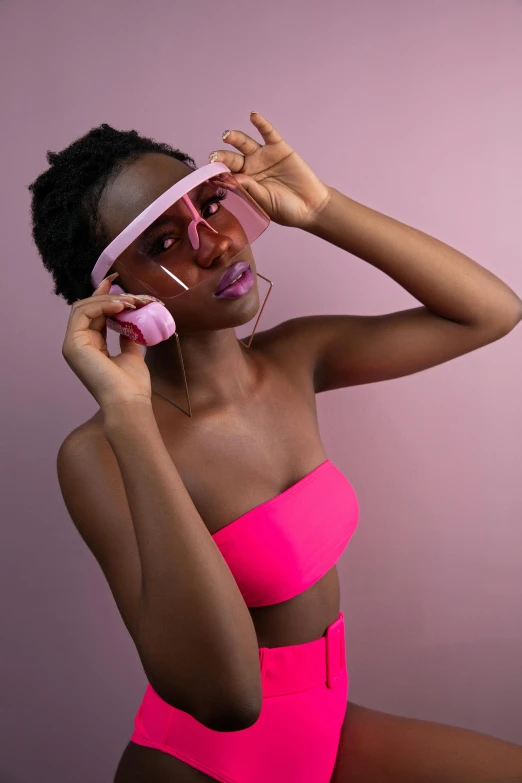 a woman in a pink bikini top and sunglasses holds up glasses while she puts her hands in her head