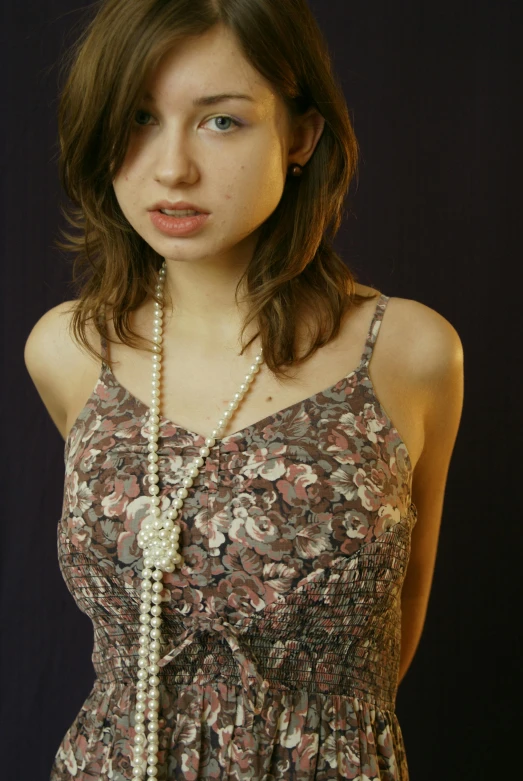a young woman wears a floral dress with a long white pearl necklace