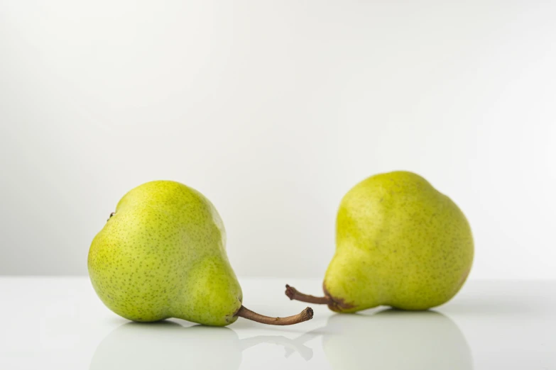 two pears on white surface one has green, the other is light colored