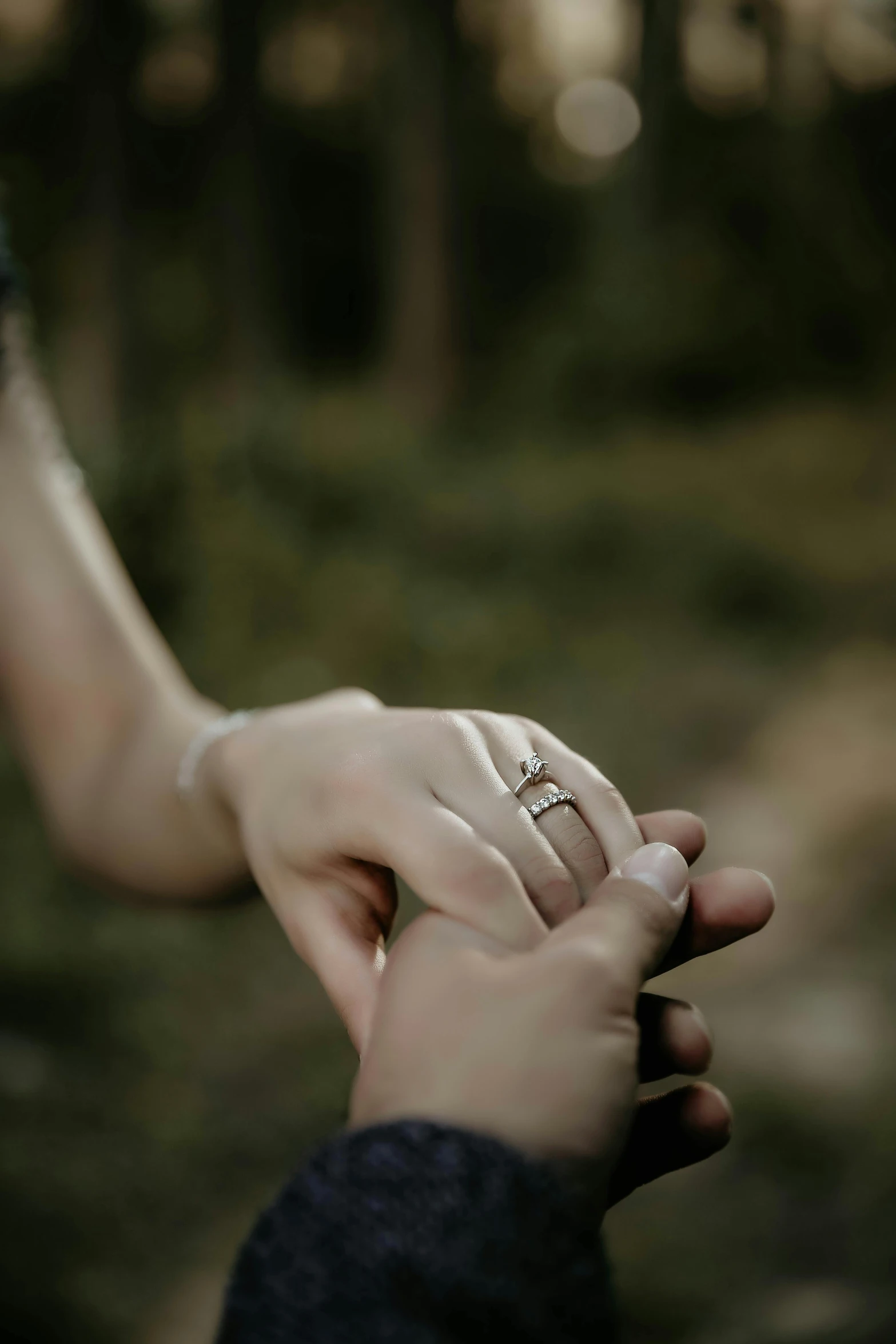 a couple holding hands in a forest during their engagement pos