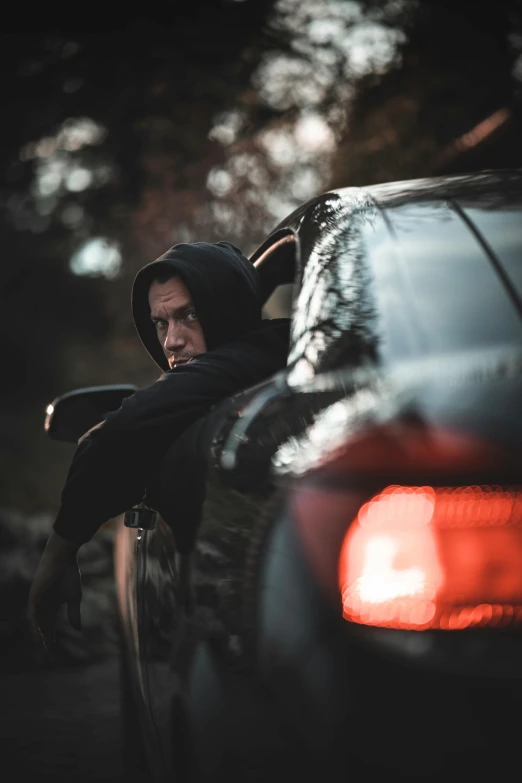 a man in hoodie leaning on a car window