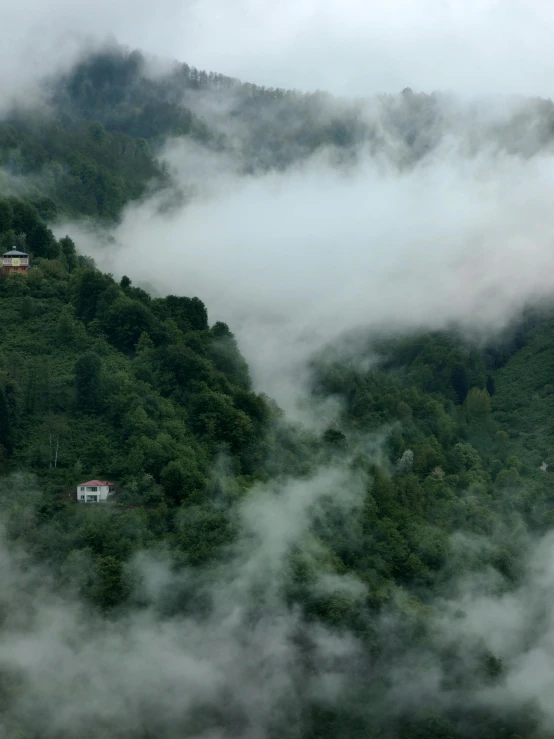 clouds surrounding houses on a mountain with some hills behind