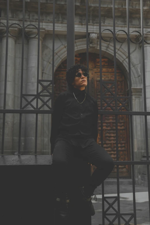 young man dressed in all black posing with an iron gate