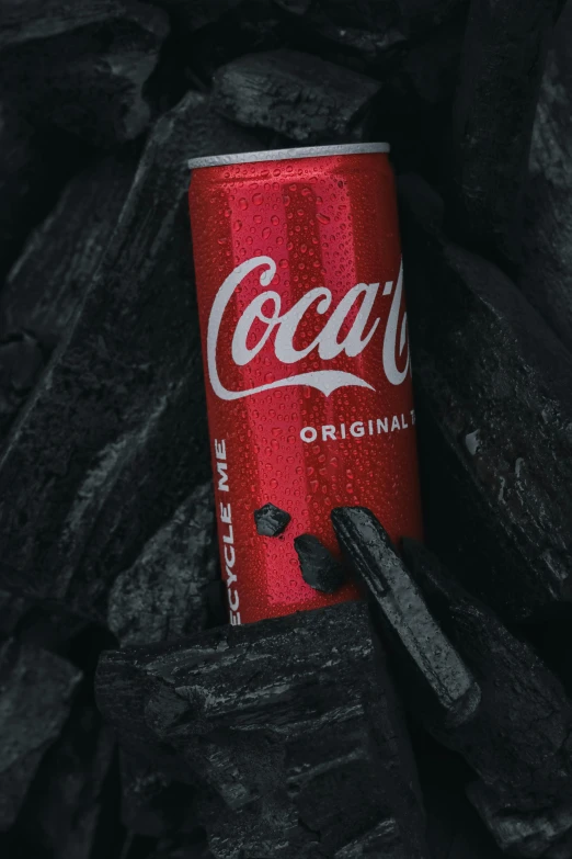 a can of soda is sitting on top of a pile of charcoal