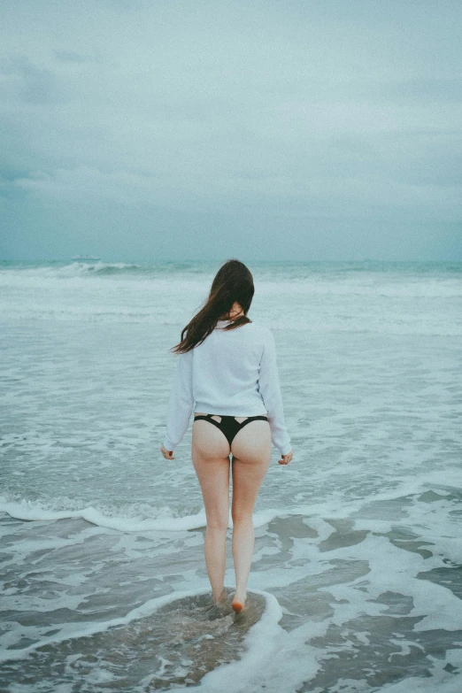 a young woman stands on a wet beach with her legs in the water