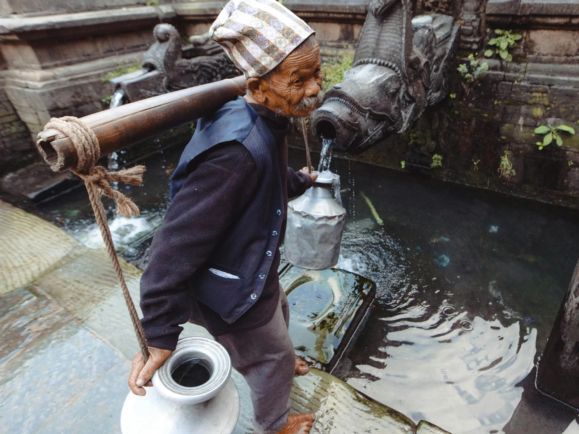 the person is carrying the large pipe next to a body of water