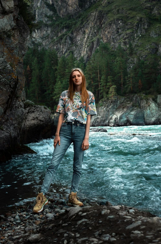 a girl stands next to a rocky river