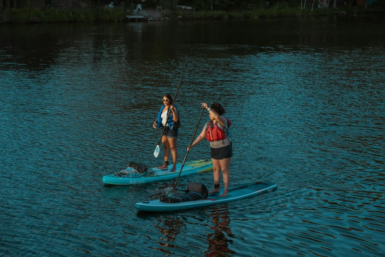 two women paddle on small surfboards in water