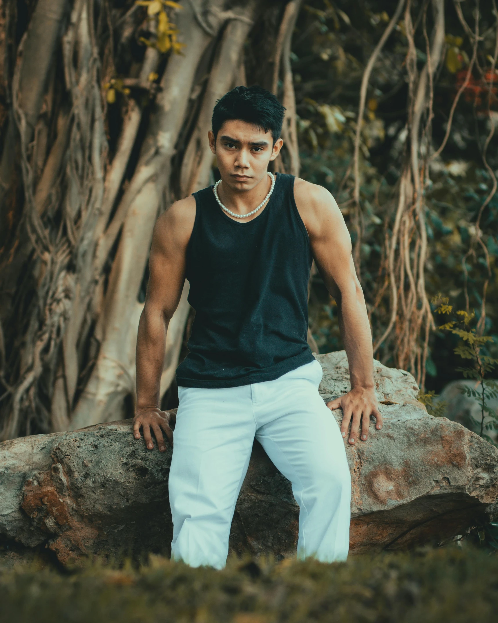 a man wearing white pants sits against a rock