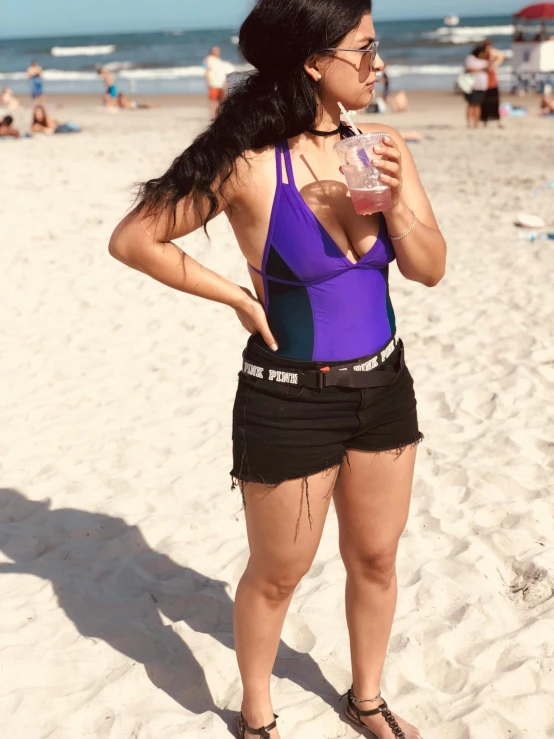 a young woman drinking a drink while standing in the sand