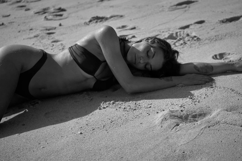 a woman laying in the sand wearing a bikini