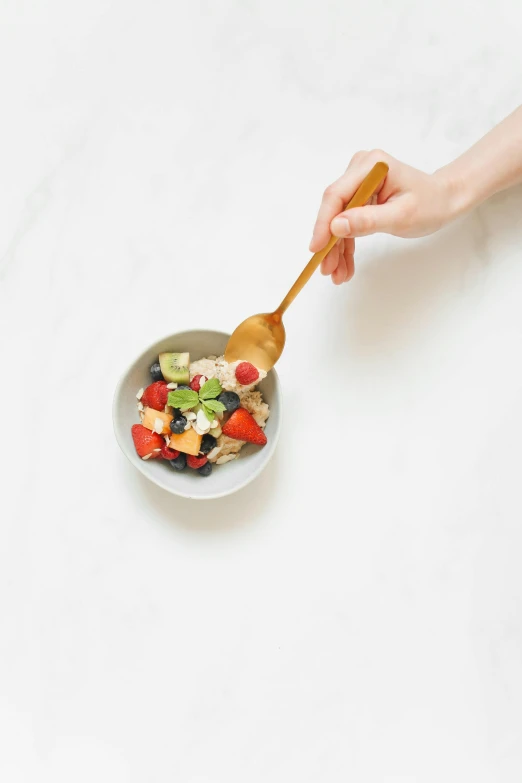 someone scooping a spoon with fruit on top of a bowl