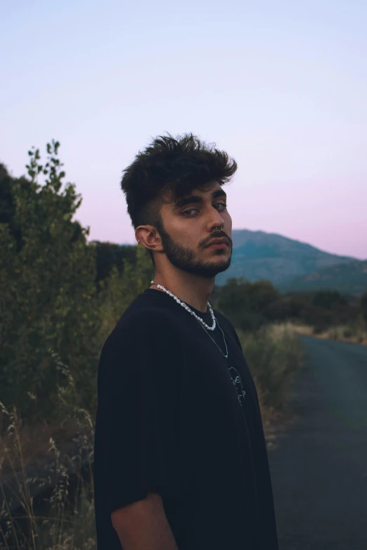 the man has dark hair and he is standing by a road