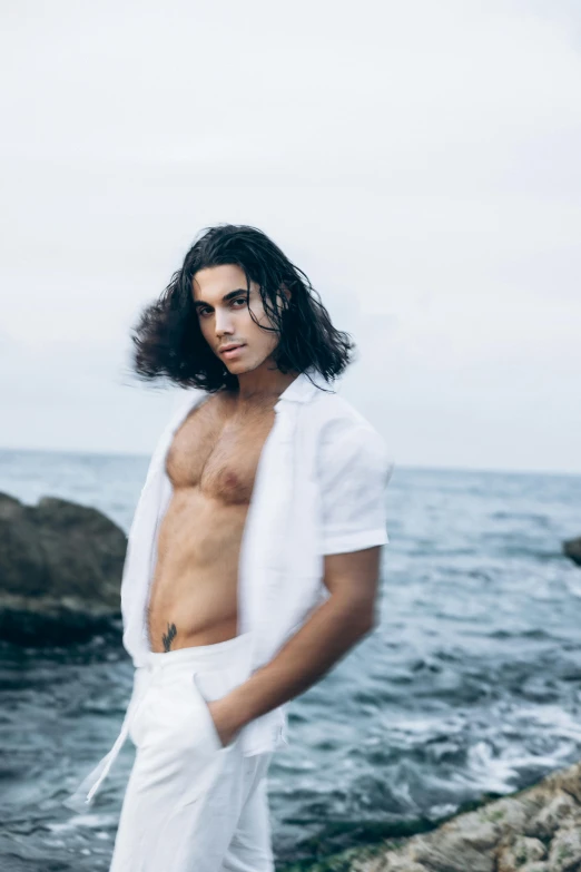 shirtless man with long hair on rocky beach