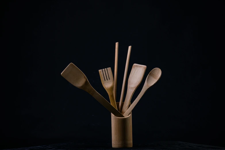 wooden utensils in a glass vase with black background