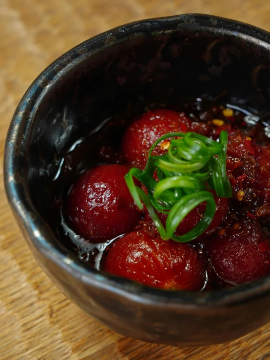 a black bowl filled with ripe fruit and topped with green stems