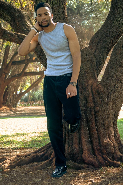 a man leaning against a tree while talking on his cell phone