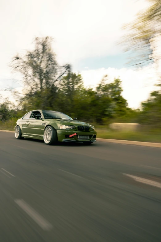 a green car driving down the road past trees