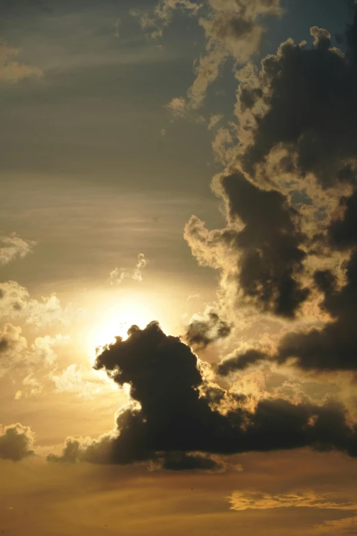 the sun peaking behind some clouds over a body of water