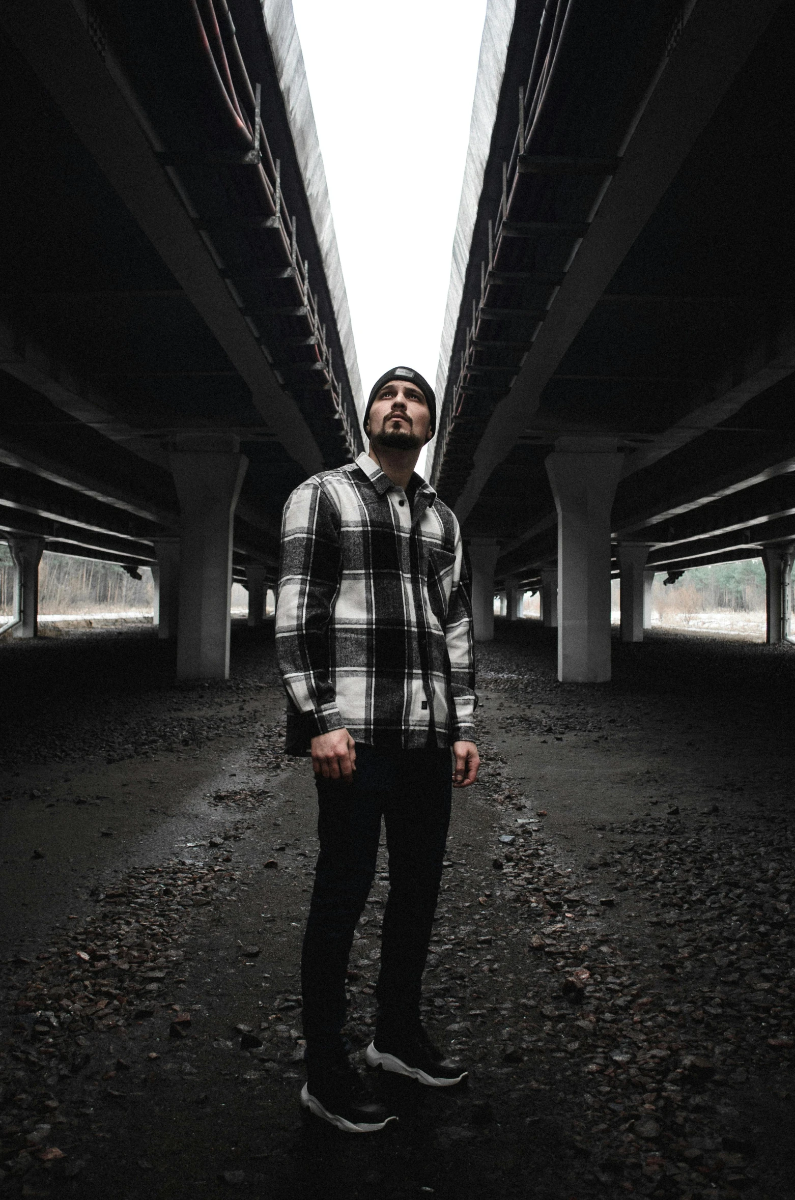 a man in plaid shirt standing under a bridge