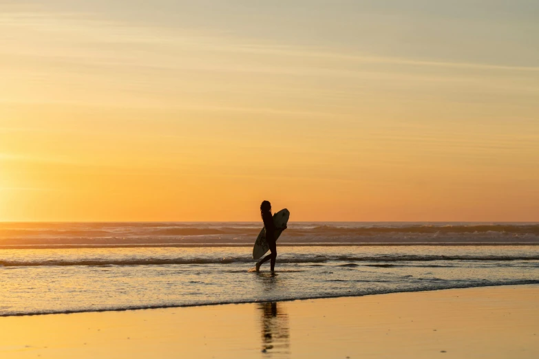 a surfer running on a beach while the sun sets