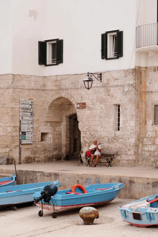 three boats parked on a concrete ground with several people sitting on a bench nearby