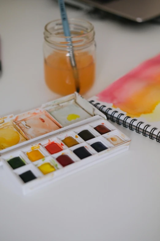 a desk with a paint palette, paint book and laptop on it